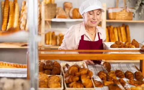 Starsza pani piekarz z uśmiechem układa świeże croissanty. To ulga dla pracujących seniorów, którzy wciąż mają pasję.