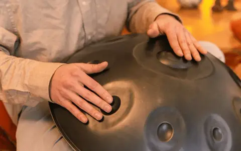Dłonie grają na instrumencie typu hang drum, tworząc kojące dźwięki.