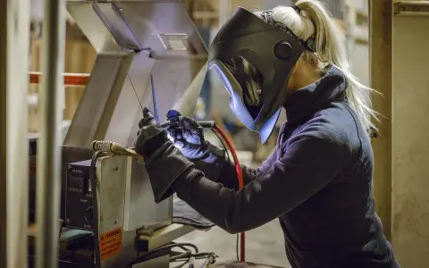 Kobieta w masce spawalniczej wykonuje spawanie w domu. Precyzyjnie łączy metalowe elementy, tworząc coś nowego.
