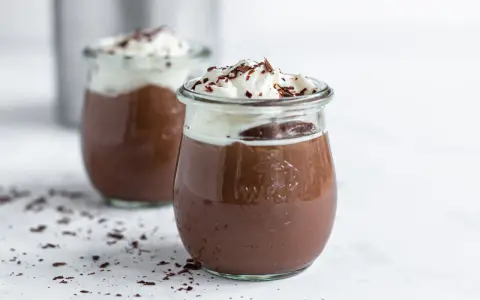 Zwei Gläser mit cremigem omas schokoladenpudding, gekrönt mit Schlagsahne und Schokostreuseln.