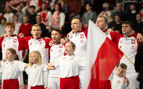 Polska drużyna piłki ręcznej z flagą narodową. Młodzi zawodnicy i dzieci w strojach biało-czerwonych.