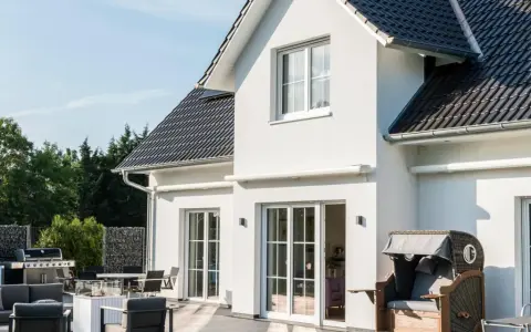 Modernes Haus mit weißen Wänden, dunklem Dach und großer Terrasse. Verschiedene haus stile sind hier vereint, von der Fassade bis zur Gartengestaltung.