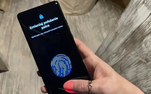 Dłoń z telefonem, na ekranie skaner linii papilarnych i komunikat "Zmieniaj położenie palca". To jak próba ucieczki z cyfrowego więzienia, niczym **jailbreak**.