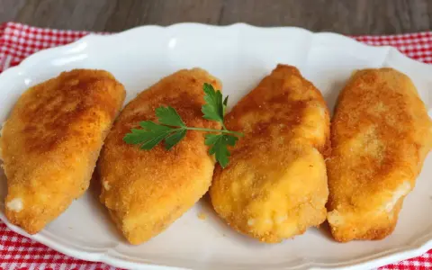 Cuatro pechugas villaroy doradas y crujientes, servidas en un plato blanco con una ramita de perejil.
