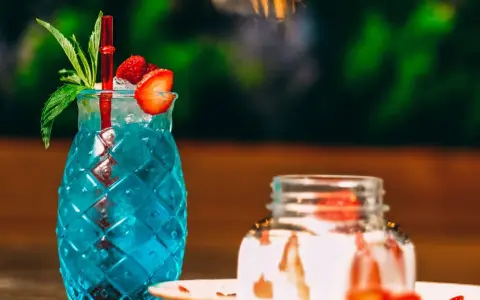 Orzeźwiający, niebieski drink z palemką, ozdobiony truskawką i miętą. Idealny na letnie popołudnie.