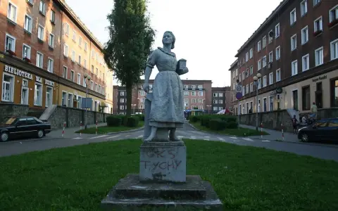 Pomnik w stylu socrealizmu na tle bloków mieszkalnych.