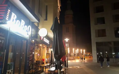 Ein beleuchtetes Restaurant "BoBoQ" und eine Kirche prägen das Bild von Dortmund bei Nacht. Menschen spazieren auf dem Gehweg, während Bauarbeiten im Hintergrund stattfinden.
