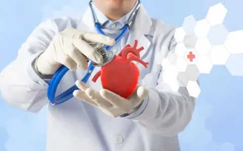 Lekarz w białym kitlu i rękawiczkach trzyma model serca, badając je stetoskopem. Grafika sugeruje, jak podwyższyć puls.