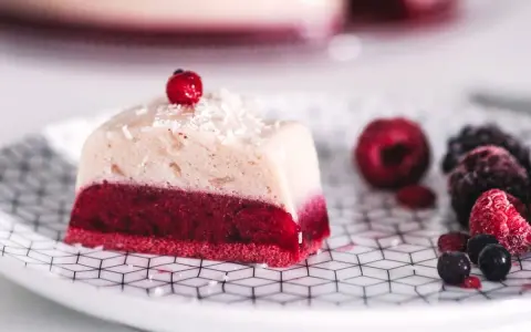 Deliciosa gelatina con agar agar, con capa roja de frutos rojos y capa superior cremosa, decorada con coco rallado y una baya.