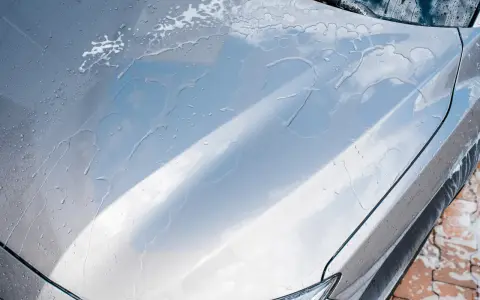Krople wody i piany na masce srebrnego auta. Czy po woskowaniu płukać auto? Tak, aby uzyskać idealny połysk.