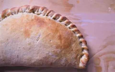 Złocisty calzone, pieczony na drewnianym tle, z charakterystycznym, zaplecionym brzegiem. Idealny na szybki posiłek.