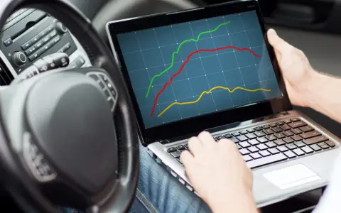 Osoba w samochodzie analizuje wykresy na laptopie, pokazujące wzrost mocy.