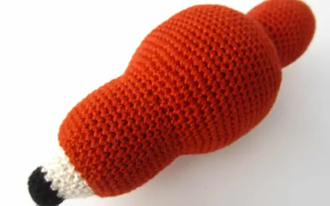 Un adorable zorro amigurumi de lana naranja, con detalles blancos y negros en el hocico, listo para jugar.