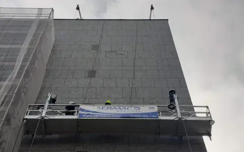 Dos trabajadores en andamios suspendidos realizan labores en la fachada de un edificio.