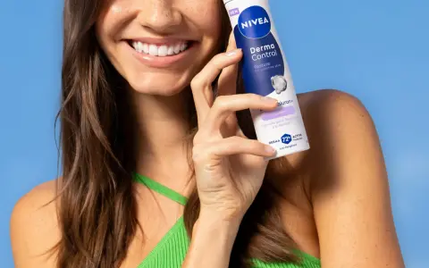 Uśmiechnięta kobieta trzymająca dezodorant Nivea Derma Control na tle niebieskiego tła.