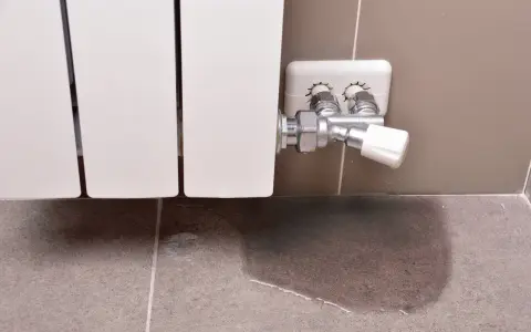 Un radiador que gotea deja un charco de agua en el suelo de baldosas, señal de un problema de fontanería.