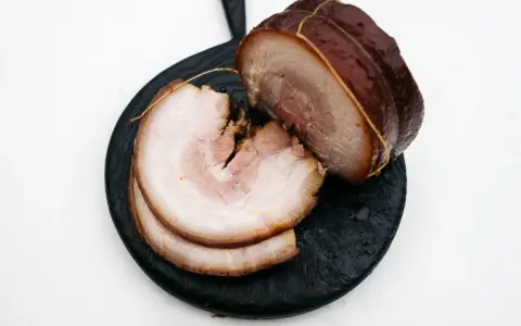 Pokrojony boczek chashu, z widocznymi warstwami mięsa i tłuszczu, ułożony na ciemnej desce.
