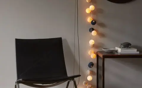 En svart läderfåtölj står bredvid ett bord med böcker och en skål. En ljusslinga med runda ljus ger en mysig inredning med ljusslingor.