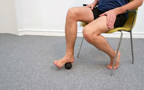 Man sitter på en stol och använder en liten boll för att rulla under foten.