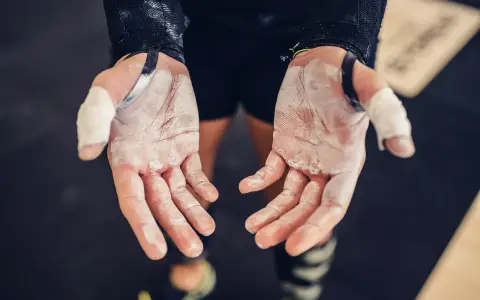 Mains de sportif couvertes de magnésie, prêtes à saisir la barre. Une corne sur la main témoigne des efforts.