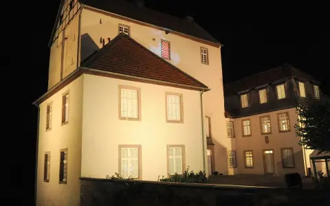 Die beleuchtete Dreckburg in Salzkotten bei Nacht. Ein imposantes Gebäude mit vielen Fenstern und einem dunklen Himmel.