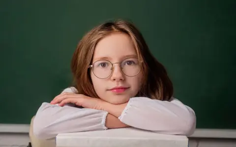 Dziewczynka w okularach opiera głowę na stosie książek. Zastanawia się, do kiedy można pobierać zasiłek rodzinny.