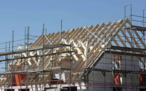 Holzkonstruktion eines Dachstuhls im Bau, umgeben von Gerüsten. Ein Architekt plant den Bau dieses Hauses.