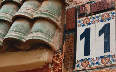 Numerologiczna 11 mężczyzna, jak liczba 11 na ozdobnej tabliczce obok zielonych dachówek, symbolizuje intuicję i duchowość.