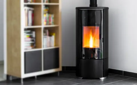 Stufa a pellet moderna in camera da letto, con fiamme vive che illuminano l'ambiente. Accanto, una libreria in legno con libri.