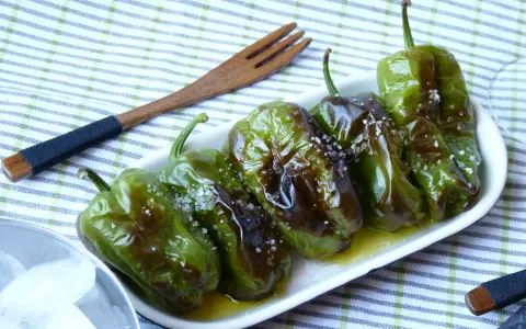 Délicieux **pieds de poivrons** verts, grillés et saupoudrés de gros sel, servis dans une assiette blanche avec une fourchette en bois.