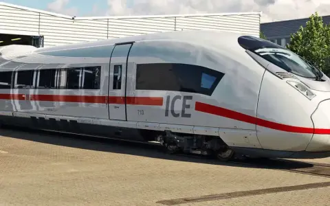 Biały pociąg ICE 5 z czerwonym pasem stoi na torach przed budynkiem.