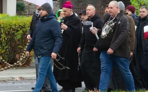 Grupa mężczyzn, w tym biskup, idzie ulicą. Niektórzy niosą różańce, jak rycerze Maryi.