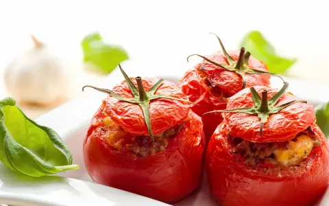Trois tomates farcies au four, garnies d'une farce savoureuse, servies avec des feuilles de basilic frais.