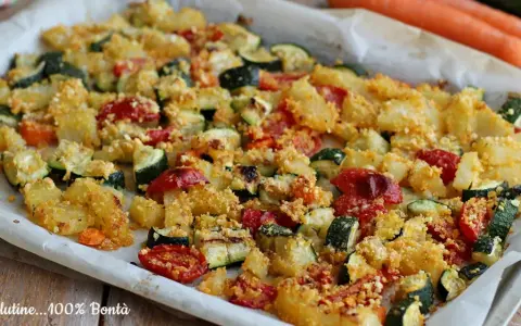 Un vassoio di verdure al forno, con patate, zucchine e pomodorini, condite con pangrattato dorato.