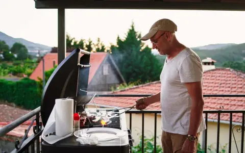 Hombre preparando barbacoa en patio interior con vistas a un pueblo.