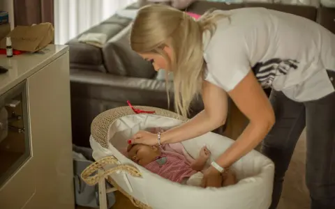 Mama delikatnie kładzie śpiące dziecko do kosza. To początek nauki samodzielnego zasypiania bez płaczu.