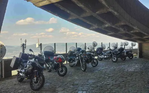 Motocykle pod betonowym zadaszeniem, z widokiem na krajobraz przypominający szwajcarskie Czechy.