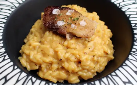 Cremoso risotto a la milanesa, coronado con un trozo crujiente y salpicado de sal marina y hierbas.