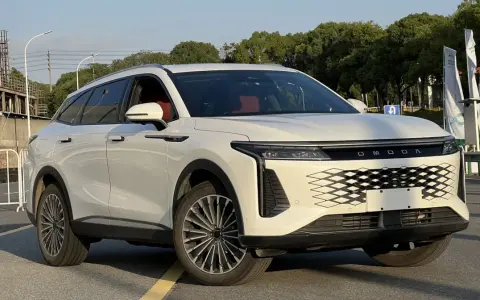 Biały OMODA 9 Super Hybrid z czerwonym wnętrzem na tle przemysłowego krajobrazu.