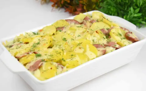 Pyszna zapiekanka ziemniaczana z kiełbasą, posypana świeżym koperkiem, w białym naczyniu.