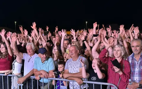 Tłum ludzi na koncercie, wszyscy z podniesionymi rękami, cieszą się muzyką. Widać uśmiechnięte twarze, a niektórzy nagrywają telefonami. To z pewnością niezapomniane **baciary utwory**!