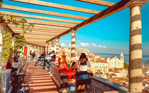 Blick vom Miradouro Lissabon über die Stadt und das Meer. Menschen genießen die Aussicht unter einer hölzernen Pergola.