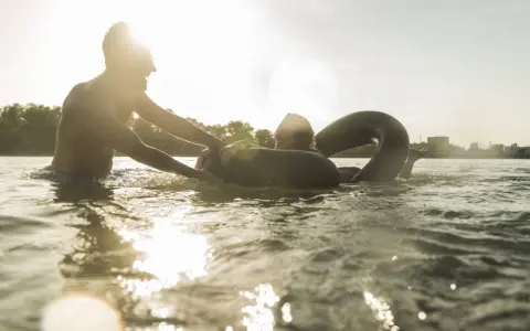 Ein Mann hilft einer Frau mit einem Schwimmring im Wasser. Ein sonniger Tag am Badesee Braunschweig.