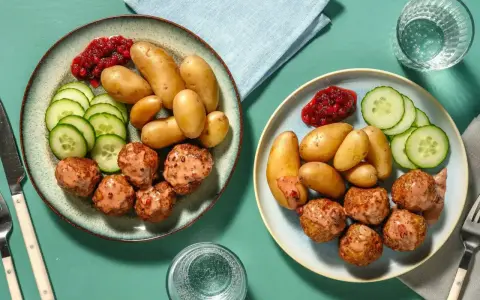 Två tallrikar med köttbullar, småpotatis, gurka och lingonsylt. En perfekt snabb middag för två.