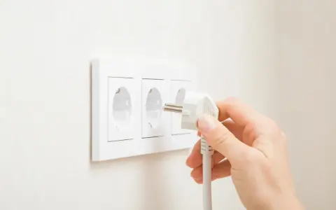 Main d'une personne branchant une prise électrique dans une prise murale triple.