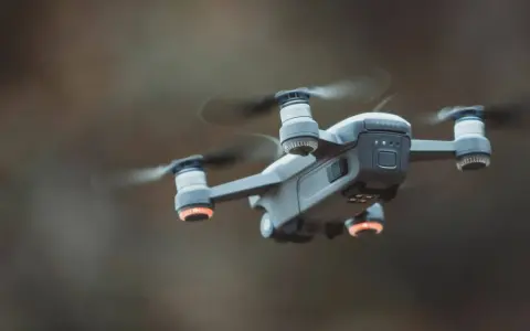 A drone hovers mid-air, its propellers a blur. Red anti-collision lights glow on its arms, ensuring safe flight.