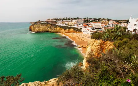 Blick auf die sonnenverwöhnte **Carvoeiro Altstadt** mit ihren weißen Häusern, die sich an die Klippen schmiegen. Der goldene Sandstrand lädt zum Verweilen ein, während das smaragdgrüne Meer sanft an die Küste brandet.