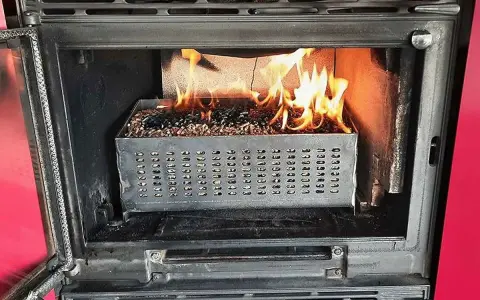 Estufa de pellets ardiendo dentro de un hueco de chimenea. El combustible se quema en una bandeja metálica perforada.