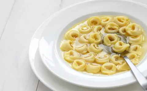 Tortellini in brodo, uno dei cibi tipici dell'Emilia Romagna, serviti in una ciotola bianca con un cucchiaio.
