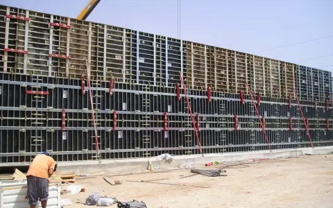 Trabajador supervisa el encofrar muro de gran tamaño, con estructura metálica y paneles negros, listo para el hormigón.